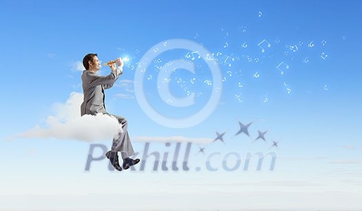Young carefree businessman sitting on cloud and playing flute