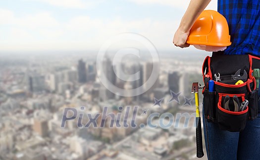 Close up of woman mechanic with yellow helmet in hand against city background