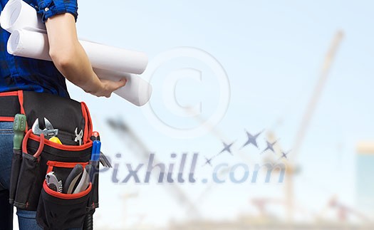 Close up of woman mechanic with yellow helmet in hand against city background