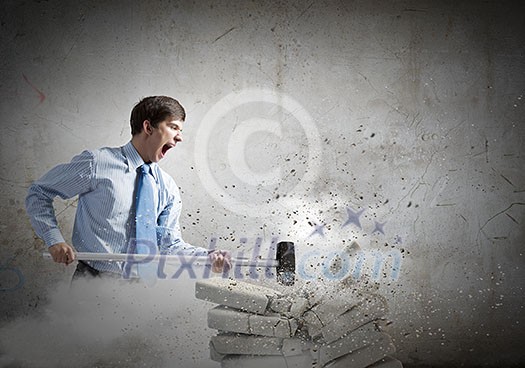Young angry businessman crashing bricks with hammer