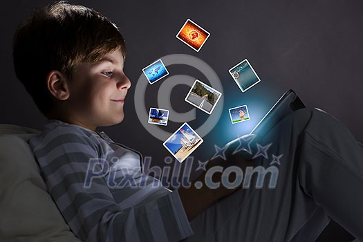 Cute little boy sitting in bed and using tablet pc