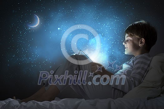 Cute boy sitting in bed and using tablet pc Cute boy sitting in bed and using tablet pc