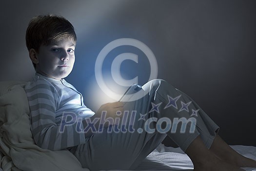 Cute boy sitting in bed and using tablet pc