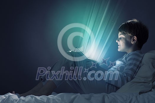 Cute boy sitting in bed and using tablet pc