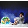 Cute boy sitting in bed and looking at Earth planet. Elements of this image are furnished by NASA
