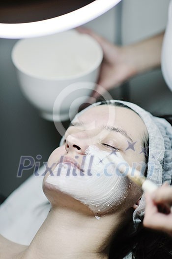 Young beautiful woman receiving cosmetic facial mask in spa beauty salon and relax