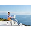 handsome young man relaxing and working on laptop computer at home balcony while looking sunset