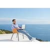 handsome young man relaxing and working on laptop computer at home balcony while looking sunset