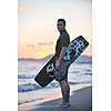 Portrait of a strong young  surf  man at beach on sunset in a contemplative mood with a surfboard