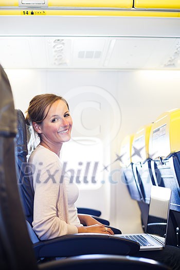 Young woman working on her laptop computer on board of an airplane during the flight