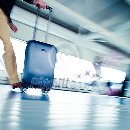 Airport rush: people with their suitcases walking along a corridor (motion blurred image; color toned image)