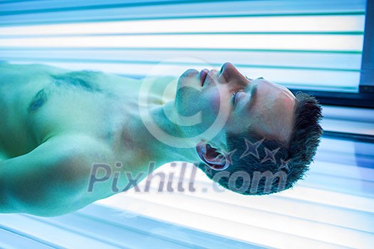 Handsome young man relaxing during a tanning session in a modern solarium Handsome young man relaxing during a tanning session in a modern solarium
