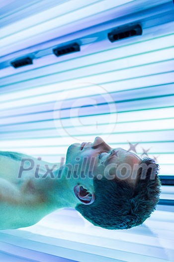 Handsome young man relaxing during a tanning session in a modern solarium Handsome young man relaxing during a tanning session in a modern solarium
