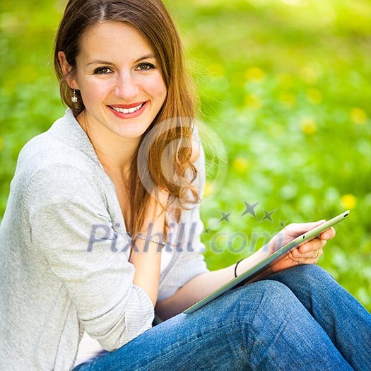 Young woman using her tablet computer while relaxing outdoors in a park on a lovely spring day