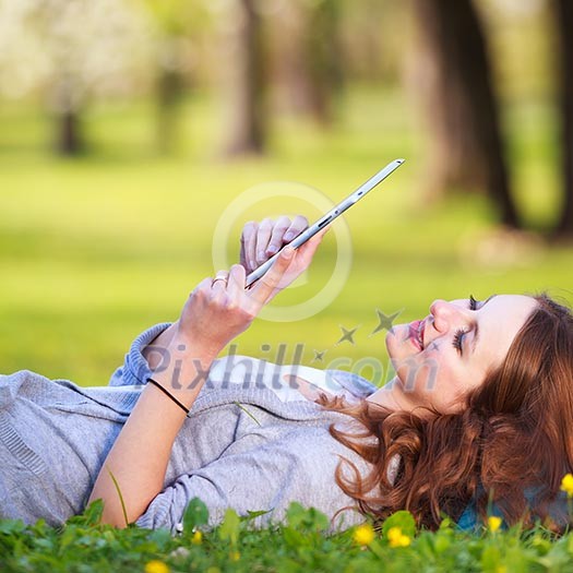 Young woman using her tablet computer while relaxing outdoors in a park on a lovely spring day