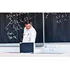 Senior chemistry professor writing on the board while having a chalk and blackboard lecture (shallow DOF; color toned image)