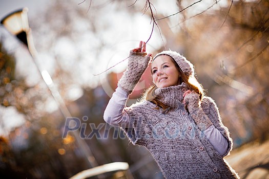 Autumn/winter portrait: young woman dressed in a warm woolen cardigan posing outside in a city park