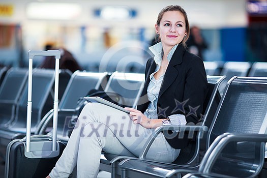 Young female passenger at the airport, using her tablet computer while waiting for her flight (color toned image)