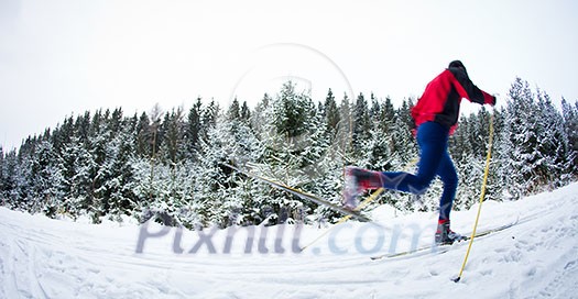 young man cross-country skiing on a snowy forest trail (motion blurred & color toned image)