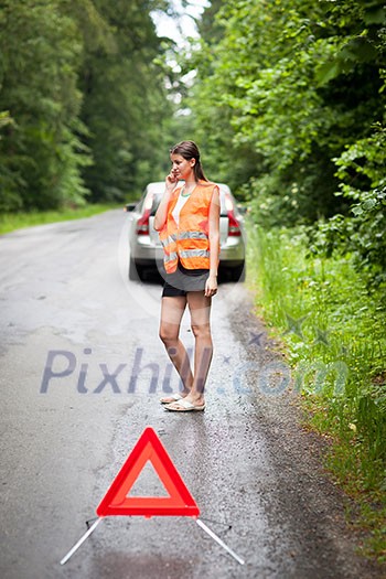 Young female driver wearing a high visibility vest, calling the roadside service/assistance after her car has broken down Young female driver wearing a high visibility vest, calling the roadside service/assistance after her car has broken down