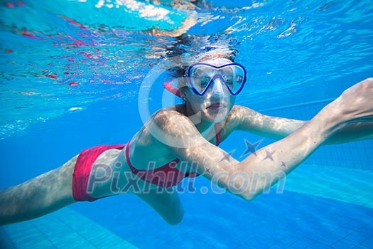 Underwater swimming: young woman swimming underwater in a pool, wearing a diving mask Underwater swimming: young woman swimming underwater in a pool, wearing a diving mask