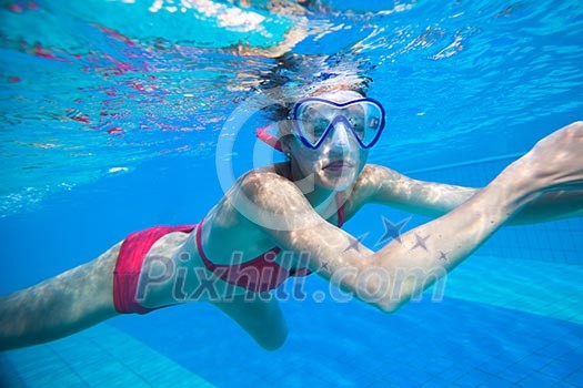 Underwater swimming: young woman swimming underwater in a pool, wearing a diving mask