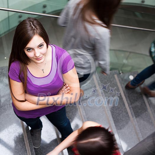At the university/college - Students rushing up and down a busy stairway - confident pretty young female student looking upwards (color toned image) At the university/college - Students rushing up and down a busy stairway - confident pretty young female student looking upwards (color toned image)