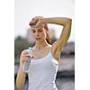 Young beautiful woman drinking water after fitness exercise and jogging outdoors