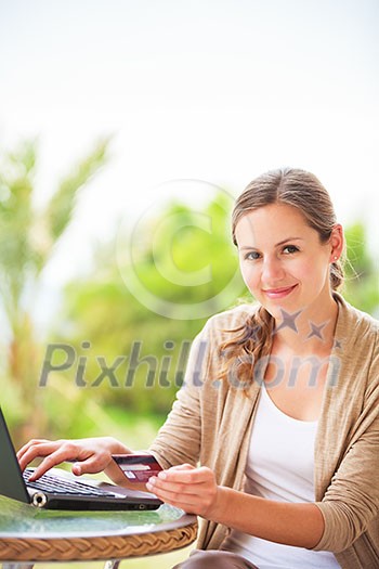 Portrait of a pretty young woman working on her computer on a terrace of her house - paying online with her credit card