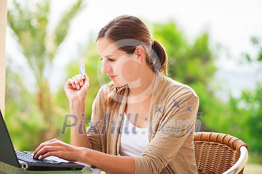 Portrait of a pretty young woman working on her computer on a terrace of her house - paying online with her credit card