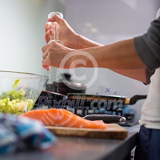 Young woman seasoning a salomn filet in her modern kitchen, preaparing a healthy food