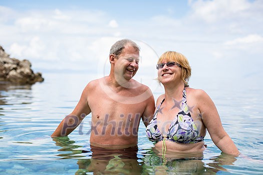 Senior couple enjoying the retirement on a seacost, having a swim in the sea, laughing togther, staying active and positive