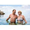 Senior couple enjoying the retirement on a seacost, having a swim in the sea, laughing togther, staying active and positive