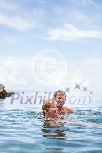 Senior couple enjoying the retirement on a seacost, having a swim in the sea, laughing togther, staying active and positive