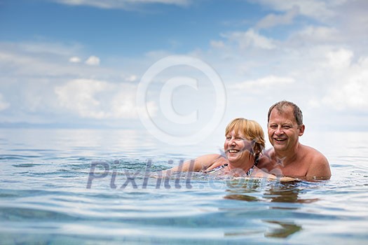 Senior couple enjoying the retirement on a seacost, having a swim in the sea, laughing togther, staying active and positive