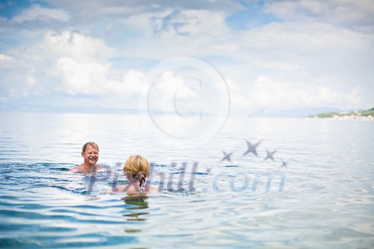 Senior couple enjoying the retirement on a seacost, having a swim in the sea, laughing togther, staying active and positive