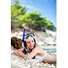 Pretty, young woman on a beach during her summer vacation with snorkel lying on beach with snorkeling mask and fins smiling happy enjoying the sun on a sunny summer day.