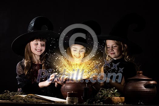 Three little Halloween witches reading spell above pot