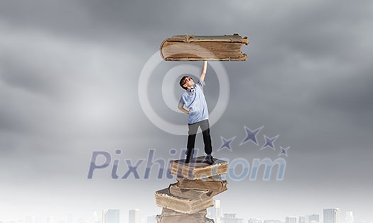 Young man holding huge book above head on one hand Young man holding huge book above head on one hand