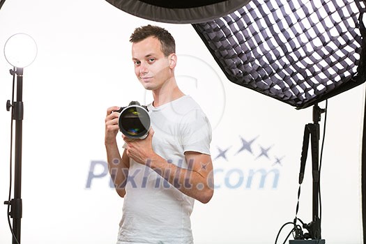 Young pro photographer with digital camera - DSLR and a huge telephoto lens in her well equiped studio, taking photos (color toned image; shallow DOF)