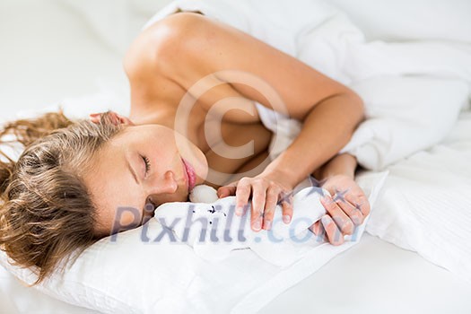 Beautiful young woman sleeping in bed, with her favorite pet toy, even though she is adult