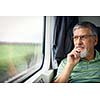 Senior man enjoying a train travel - leaving his car at home, he savours the time spent travelling, looks out of the window, has time to admire the landscape passing by