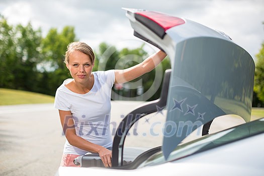 Young, attractive, happy woman taking a suitcase from her car's trunk, smiling, enjoying the travel experience