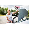 Young, attractive, happy woman taking a suitcase from her car's trunk, smiling, enjoying the travel experience