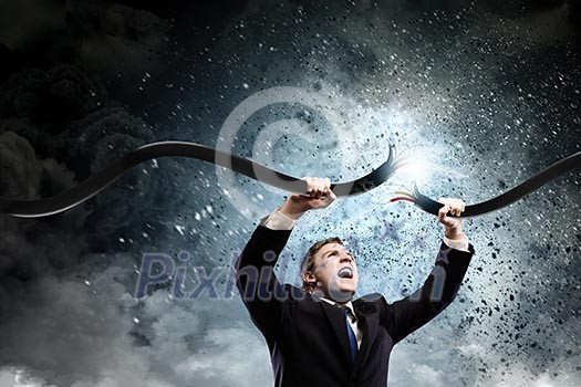 Young businessman tearing electricity cable with hands Young businessman tearing electricity cable with hands