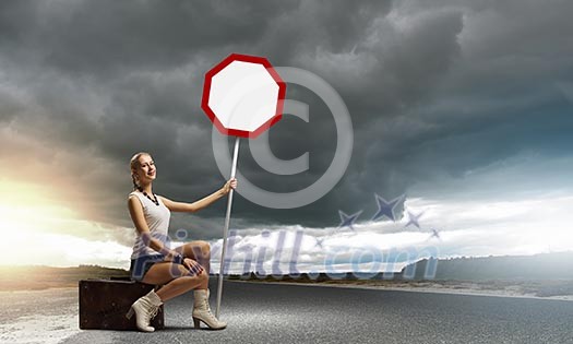 Young woman with road sign sitting on suitcase