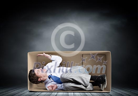 Young frustrated businessman sitting in small carton box