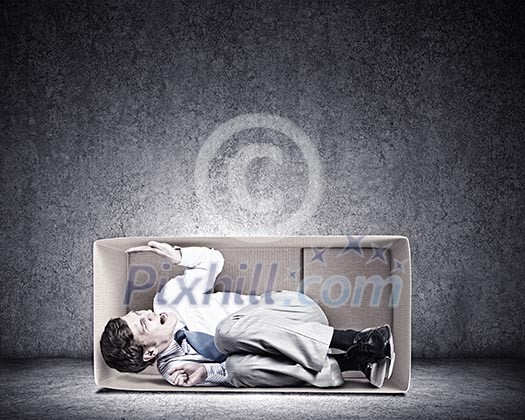 Young frustrated businessman sitting in small carton box
