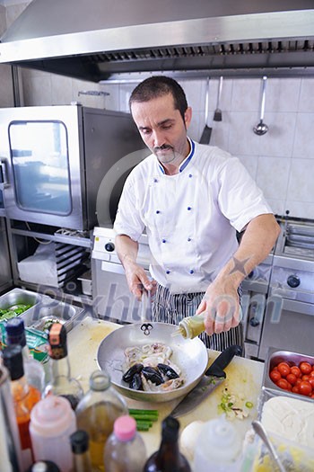 Handsome chef dressed in white uniform decorating pasta salad and seafood fish in modern kitchen