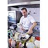 Handsome chef dressed in white uniform decorating pasta salad and seafood fish in modern kitchen